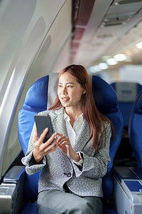 一位微笑的亚洲女商人在飞机上使用手机的肖像