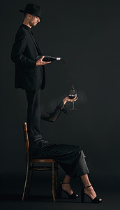 一位英俊的年轻男子穿着得体，在黑色背景下的工作室里，将红酒倒进一位面目全非的女人的酒杯中。