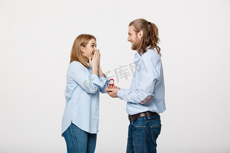 提案概念-男人在孤立的白色背景下向他美丽的女朋友展示订婚戒指钻石的肖像。
