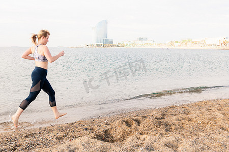 金发女运动员沿着城里的海滩跑步