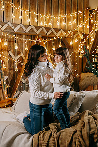 一个小女孩和她的母亲在舒适的家庭环境中，坐在圣诞树旁边的沙发上。