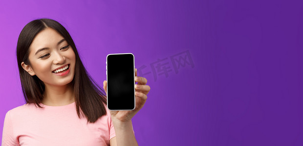 高兴的快乐漂亮的亚洲年轻女性微笑着满意地拿着智能手机，显示手机屏幕看起来手机显示很高兴，介绍应用程序，展示应用程序，紫色背景