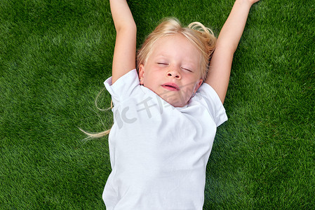 肖像可爱的金发女孩闭着眼睛躺在绿草上。