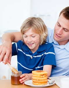 可爱的男孩和他的父亲把蜂蜜放在华夫饼上