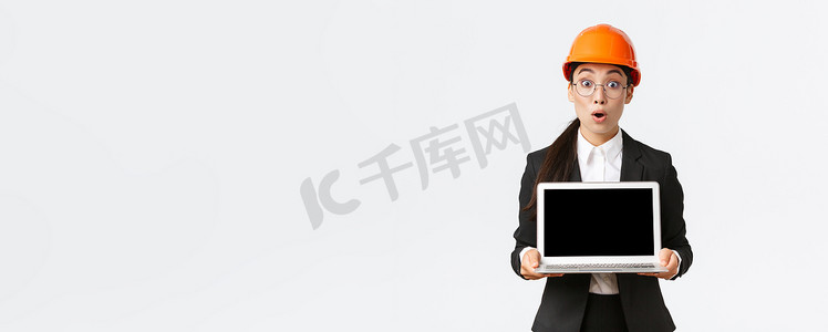令人印象深刻和兴奋的亚洲女工程师在图表上展示惊人的结果，安全头盔和西装的工业技术人员展示笔记本电脑屏幕，表情惊奇，白色背景