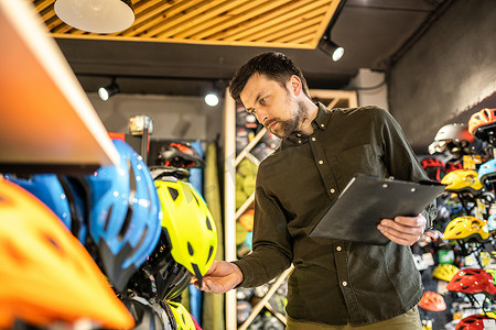 自行车店经理在平板电脑上查看头盔价格信息，卖家在体育用品店盘点。