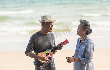 快乐的老年夫妇在阳光明媚的海边海滩放松，在户外唱歌和弹吉他