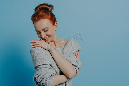 穿着针织毛衣的年轻美丽浪漫的红发女人高兴地拥抱自己
