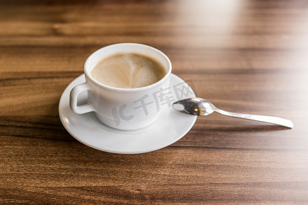 咖啡馆桌子的木质背景上放着一杯热咖啡，碟子上放着勺子