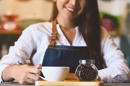 加奶咖啡杯特写镜头有美丽的亚洲女咖啡师背景的为顾客服务。