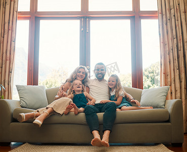 年轻快乐满足的白种人家庭拿着纸板作为屋顶覆盖他们坐在家里的地板上。