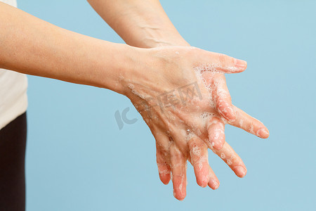 上洗手摄影照片_女人在蓝色背景上用肥皂洗手。