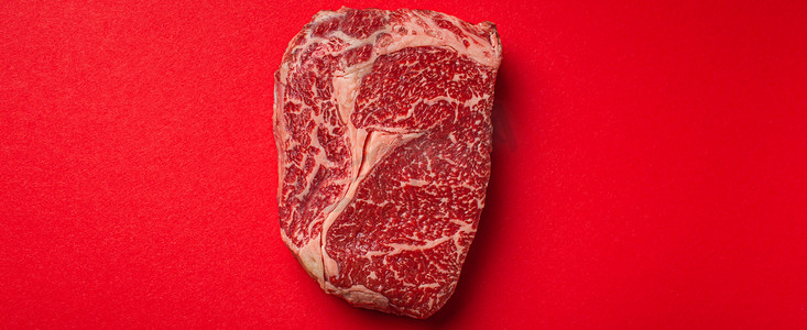 极简主义背景摄影照片_生肉牛肉优质切牛排肋眼从上面干净的红色背景，牛排概念横幅极简主义