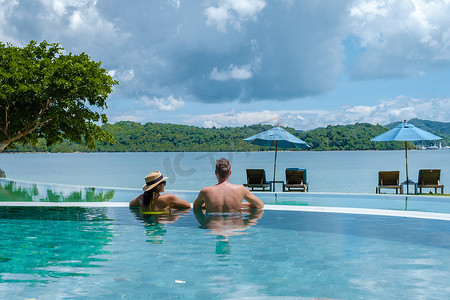 一对欧洲男人和亚洲女人在泰国的无边泳池里眺望大海，在泰国享受豪华假期