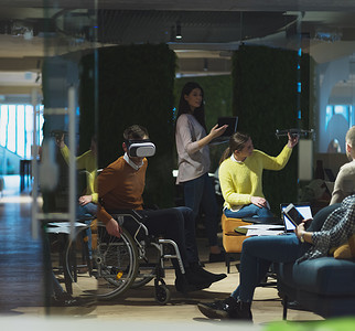 坐在轮椅上的残疾商人在现代开放空间联合办公室工作，团队使用虚拟现实谷歌无人机辅助模拟