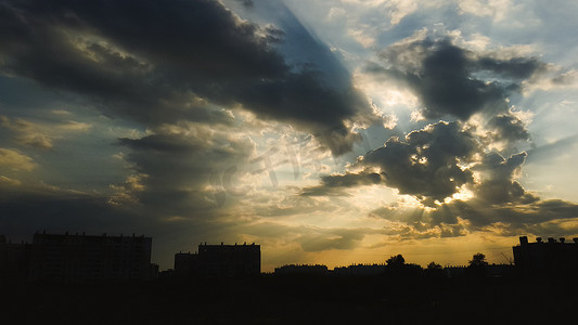 太阳在云层后摄影照片_云层后面的太阳将阳光投射在建筑物剪影上方的美丽天空上