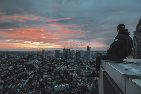 大约2018年6月:坐在屋顶边缘的人俯瞰德国美因河畔法兰克福夜间天际线