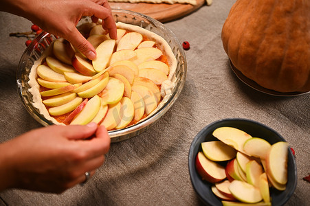 女人的手的特写镜头，将苹果片围成圆圈放在生南瓜派上。