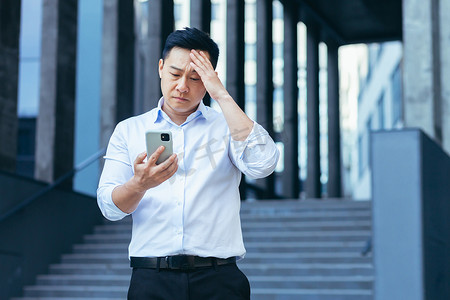 心烦意乱的亚洲商人从手机屏幕上读新闻，男人对坏消息感到失望
