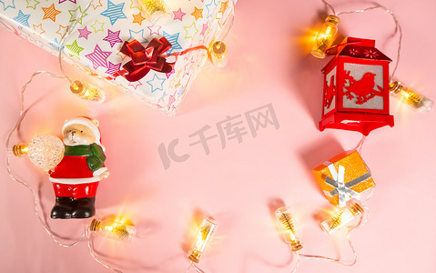 圣诞节背景-圣诞节装饰品-花环、礼品盒、手电筒和浅粉色背景上穿着圣诞老人服装的熊，复制空间。