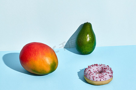 双色背景摄影照片_双色背景下新鲜水果和糖果、甜甜圈芒果和鳄梨的组合物