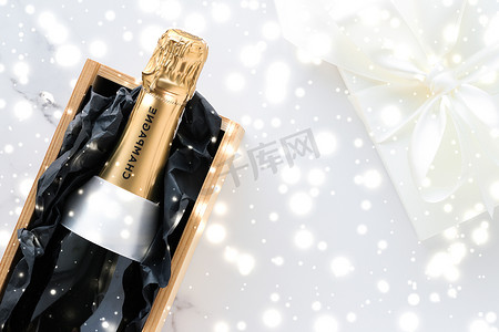 圣诞假期香槟瓶、礼盒和大理石背景上闪亮的雪
