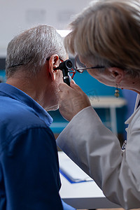 医护人员使用耳镜对柜内老年患者进行耳部检查的特写