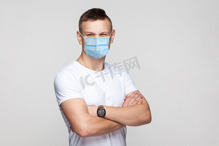 戴着医用口罩的男子双臂交叉站着，用滑稽的表情看着镜头眨眼。