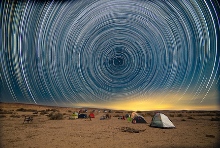 沙漠帐篷露营摄影照片_夜间沙漠营地上空的星轨