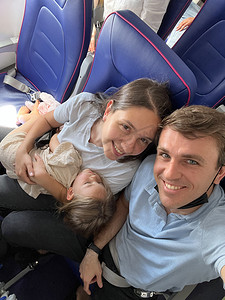 在飞机上睡觉摄影照片_爸爸和妈妈抱着熟睡的女儿坐在飞机座位上