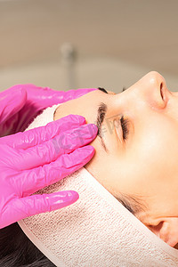 戴着手套的美容师在女性脸上涂上带去角质霜的保湿面膜。