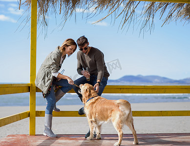 狗狗吃东西摄影照片_年轻夫妇带着狗在海滩上