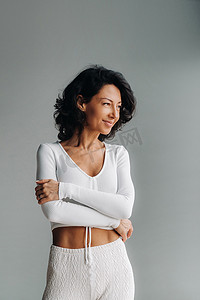 健身教练摄影照片_灰色背景中突出显示的一位身穿白色运动服的欢快微笑女性的画像