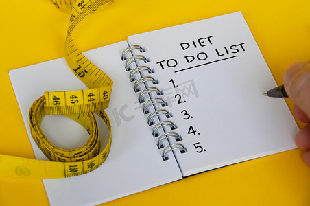 白色记事本上的饮食计划文本，黄色背景上有卷尺。