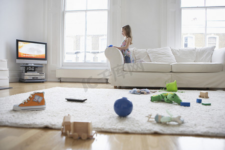 一个小女孩在前景地板上放着玩具看电视的侧视图