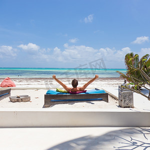 在豪华躺椅上放松的人，举起双臂，在美丽的海滩上享受暑假。