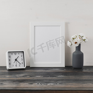白色框架，花在迷雾中，深灰色木桌上的时钟靠在白色的墙上，有复制空间。