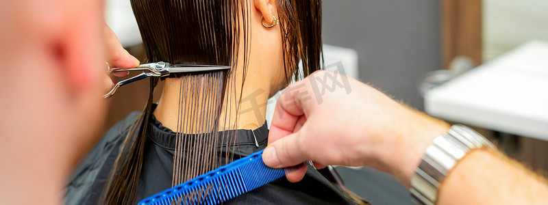 美容院里，男理发师用剪刀和梳子给女顾客剪头发。