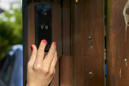 按门铃手摄影照片_女人的手按花园木栅栏上的门铃