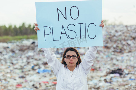 海报保护环境摄影照片_女志愿者在垃圾填埋场举着无塑料海报，积极分子与环境污染作斗争