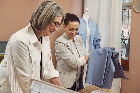 一位中年西班牙裔时装设计师的肖像，穿着一件时尚的夹克，拿着蓝色面料，在时装设计工作室创造了一个新的女式衬衫系列