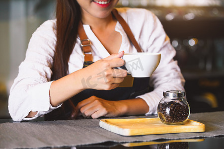 手自助服务摄影照片_加奶咖啡杯特写镜头有美丽的亚洲女咖啡师背景的为顾客服务。
