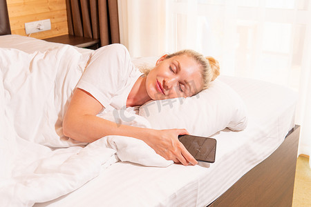 女人美丽的金发手机睡眠床毯视图早晨，成人枕头从梦中快乐的午睡，积极的光线。