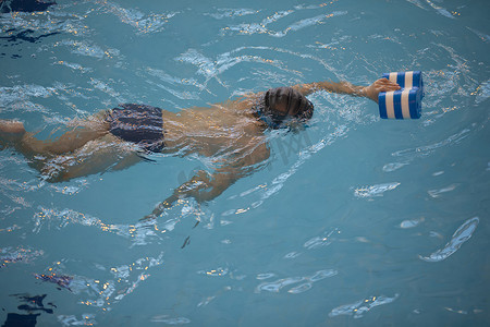 游泳泳镜摄影照片_游泳池里戴着泳帽和泳镜的男孩。