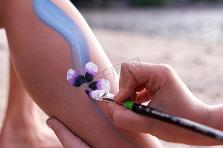 艺术家在海滩上一个女人的腿上画一朵花
