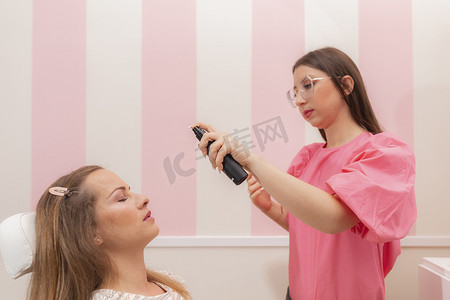 一位美容师在美容院为她的顾客涂抹粉底喷雾