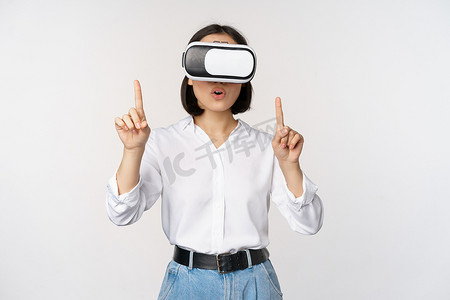 戴着 vr 眼镜的亚洲女性手指向上的形象，看起来既惊讶又惊讶。