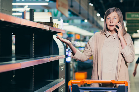 一家超市里空荡荡的货架附近没有商品的高级妇女感到震惊和不安