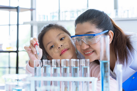 科学家女孩和老师一起用吸管将溶液物质液体滴入实验室教室的试管中。