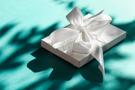 礼盒绿色摄影照片_翠绿背景上带丝带和蝴蝶结的豪华假日白色礼盒、豪华婚礼或生日礼物